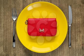 Savings consumer concept.Red purse on the yellow plate with fork and knife.