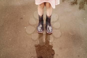 Child wearing  rain boots walking into a puddle