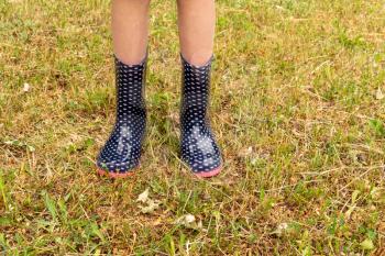 Child legs on a wet lawn wearing rain boots