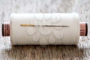  Spool of white thread with a needle on wooden background