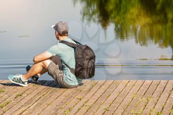 Back view of man with backpack sitting on a pier