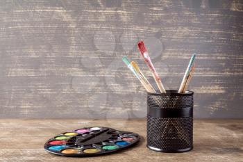 Watercolor palette and pot with brushes on  wooden background