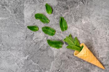 Wafer cone with mint leaves on grey stone background