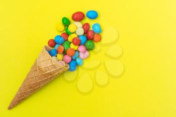 Waffle horn with colored candy on yellow background