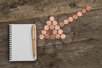 Combination of coin arrow and blank notebook on wooden background