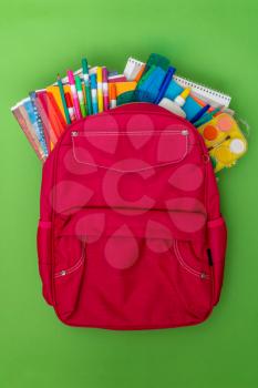 Back to school concept. Backpack with school supplies on the green background.