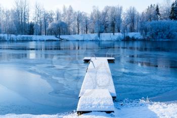 Snow covered wooden pier over the frozen lake in the forest
