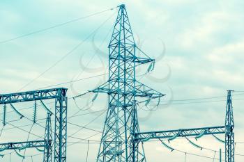 High-voltage power lines. Distribution electric substation with power lines and transformers. Blue filtered image.
