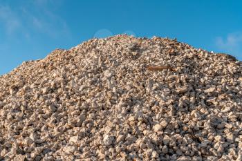 Industrial background with pile of gravel in front of the blue sky. Extraction of gravel. Construction of roads. Pile of gravel on construction site.