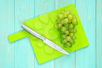 The branch of green grapes with a knife on a cutting board