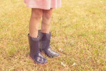 Legs of girl standing on a wet lawn wearing rain boots