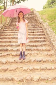 Child girl with umbrella stands on the stairs