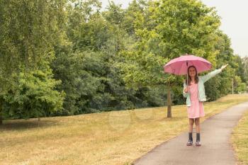 Child girl with umbrella under rain walking in a park