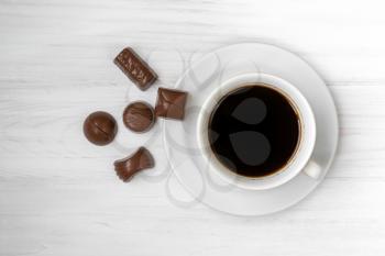 Cup of black coffee with chocolate candies on white wooden background