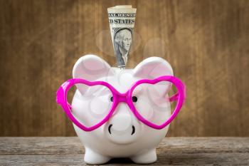 One dollar banknote in a piggy bank wearing a pink glasses