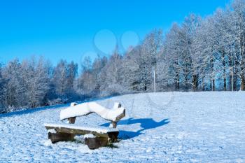 Winter landscape with deserted bench covered in fresh snow