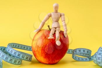 Wooden man doll sits on the red apple with measure tape.
Healthy life concept.