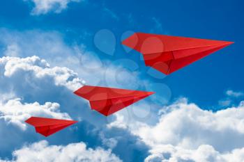 Red paper planes flying in a cloudy sky. Travel concept.