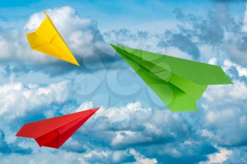 Three colorful paper planes flying in a cloudy sky. Travel concept.