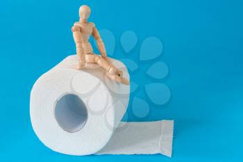 Wooden figure sit on a roll of toilet paper. Concept of the problem with digestion.