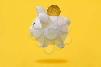Piggy bank with bitcoin coin levitating over a yellow background