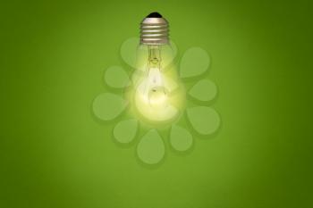 Light bulb glowing on green background. Eco energy concept.