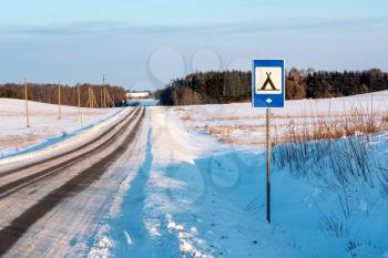 Snowy country road with blue road sign of camping