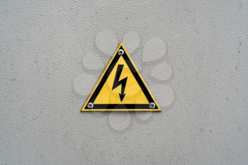 High voltage yellow triangle warning sign on gray metal wall. Danger electricity warning sign. Black lightning arrow symbol on yellow background in triangle.