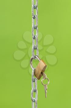 Gold padlock with key and chain on green background