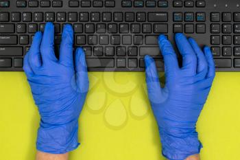 Closeup of black computer keyboard and hands in blue medical gloves. Work from home covid-19 concept.