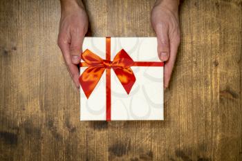 Man hands holding present box with red bow on wooden background. Flat lay style.