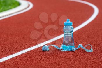 Plastic bottle of water with measure tape on running track at stadium