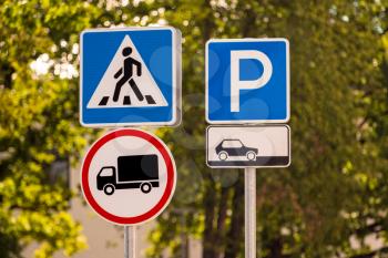 Traffic signs: pedestrian crossing, no goods vehicles, car parking. Road signs with blurry trees background