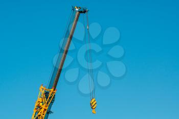 Part of a mobile hydraulic crane, the hook of a crane without a load on the background of blue sky. 