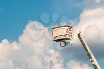 Aerial work platform lifted up against blue sky with clouds