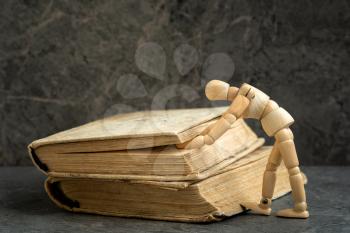 Wooden man trying to open book. Dummy looking for something in books. Literature research. Concept - information search in books. 
