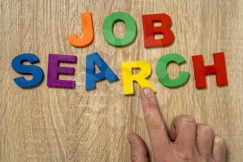 Job Search - color plastic letters and human hand  on the wooden desk