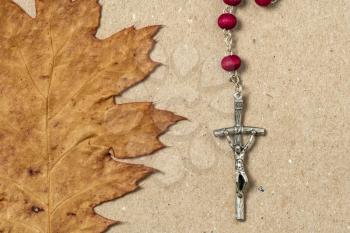 Close-up view of catholic rosary and dry maple leaf.