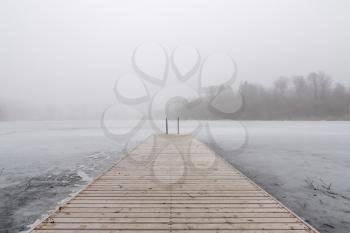 Wooden jetty on foggy day by the lakeside during winter