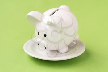 Savings consumer concept. White plate with piggy bank on green background