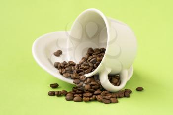 White cup filled with roasted coffee beans falling on a green background