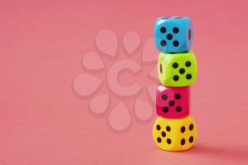 Stack of colorful dice on pink background. Copy space.