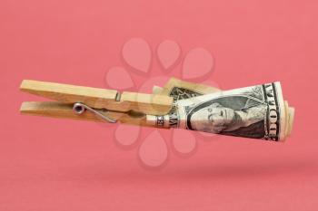 Wooden clothes pin with one dollar floating over pink background