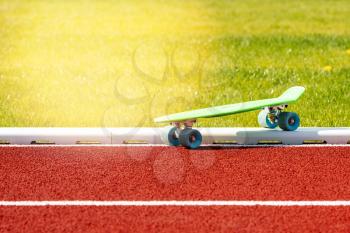 Green skateboard stands on the running track in the school stadium