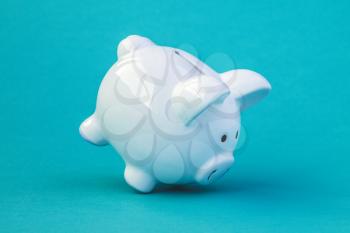 White ceramic piggy bank falling on blue background