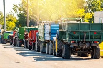 Tractors delivering recently harvested grain, stretching along the road