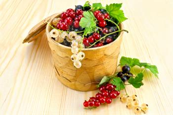 White, red and black currant with green leaves in a bowl  from birch bark on a wooden board