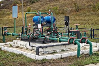 Blue cylinders, green with red edging pipe group metering device of the pipeline on the black and white based on the background of yellow-green grass and bushes