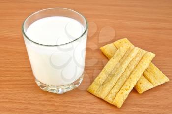 Milk in a glass, golden bread on background a wooden board