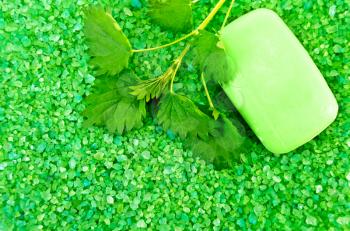 The texture of green bath salts with a bar of green soap and a sprig of nettle